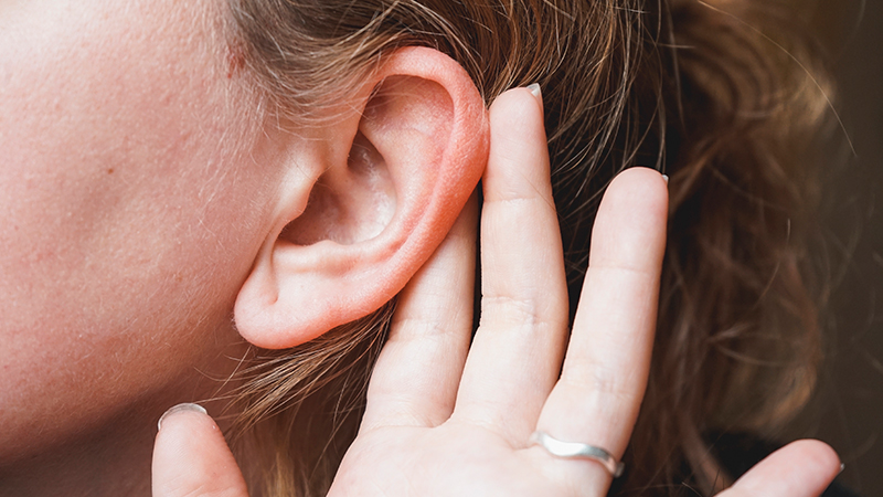 A woman holding her ears out. Otoplasty (protruding ears) concept.