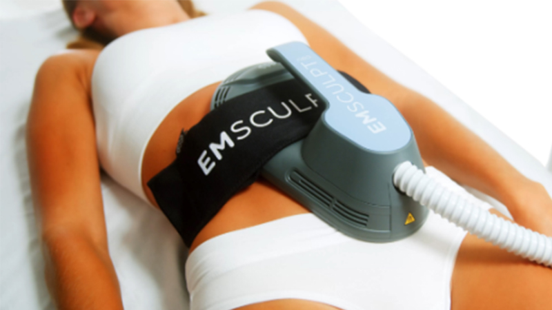 A woman receives an Emsculpt NEO treatment. The machine is strapped to her abs.