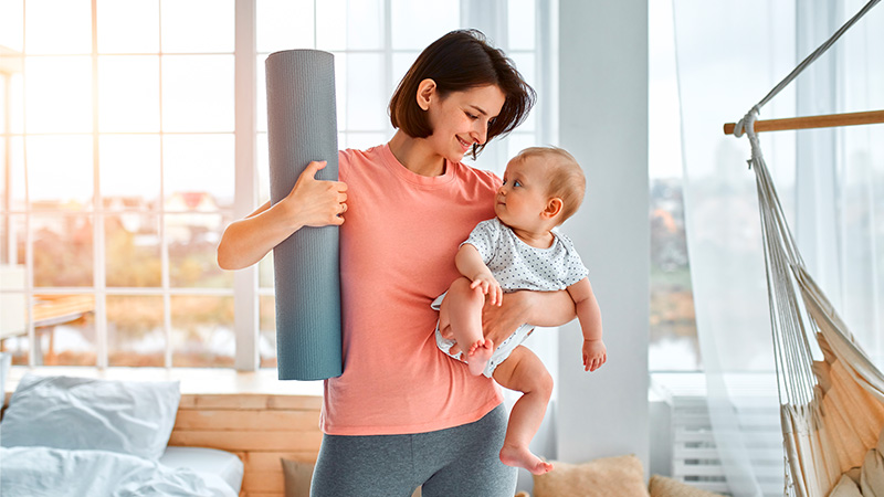 A mom holding her baby and a yoga mat. Mommy makeover concept.
